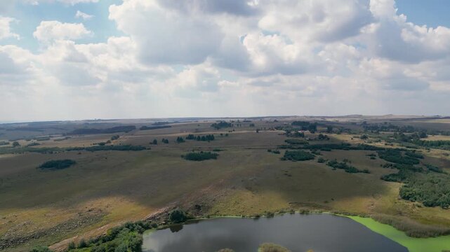 High altitude drone reveal tilting down to show a lake surrounded by the endless rolling highveld grasslands of Ermelo, South African