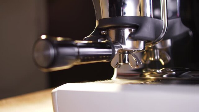A hand inserts a portafilter into the grinder mount of a sleek stainless steel espresso machine. The close-up highlights the moment of preparation in a premium, softly lit coffee-making environment.