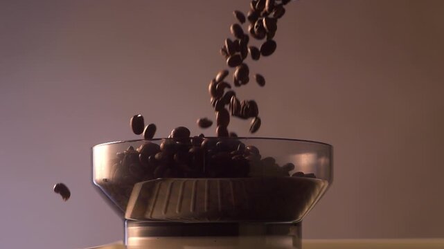 Coffee beans fall in slow motion into the hopper of a portafilter machine or espresso grinder. The cinematic close-up captures the flow and bounce of the beans against a soft gradient background.