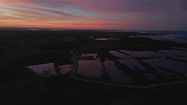 Right-side drone perspective showing a long rural road cutting through rice fields during sunset in Anda, Pangasinan.