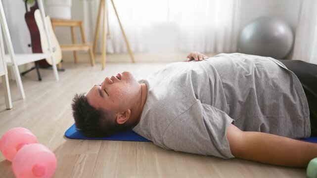 Exhausted Asian plus-size man lying down on a yoga mat after workout.