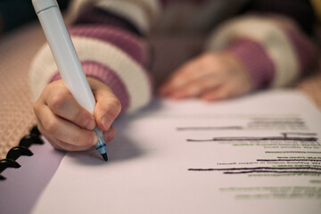 Caucasian child writing on paper with marker, hand holding pen while crossing out text, wearing...