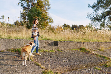 Naklejka premium Woman walking a dog along a gravel path in a sunny park, casual attire, relaxed outdoor activity, nature in the background, everyday companionship