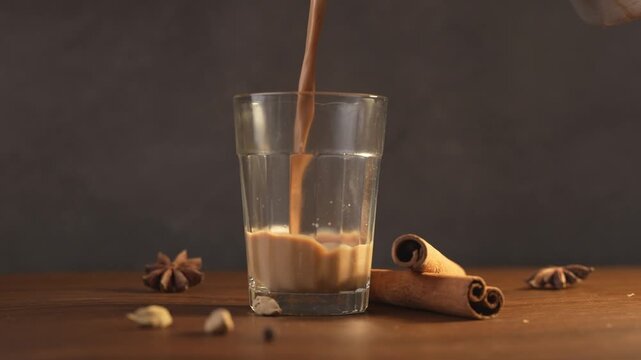 Indian chai served in glass cups, brewed in a metal kettle with aromatic masalas. Getting poured on glass.