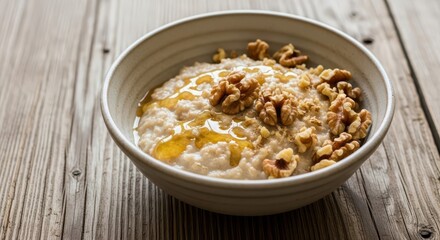 Creamy warm porridge topped with honey and shelled nuts rests on a weathered wooden surface