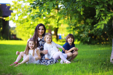 Fototapeta premium Young large family on a summer morning walk. Beautiful mother with children is playing in the park.