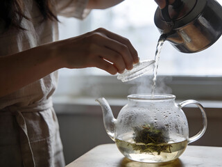 Woman pouring hot water into glass teapot with herbs for tea graphic design