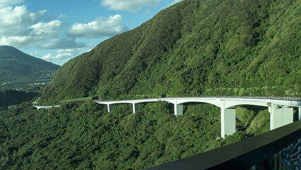 八丈島の険しい山肌に沿って曲線を描く白い大坂橋と周囲を覆う深い緑の原生林