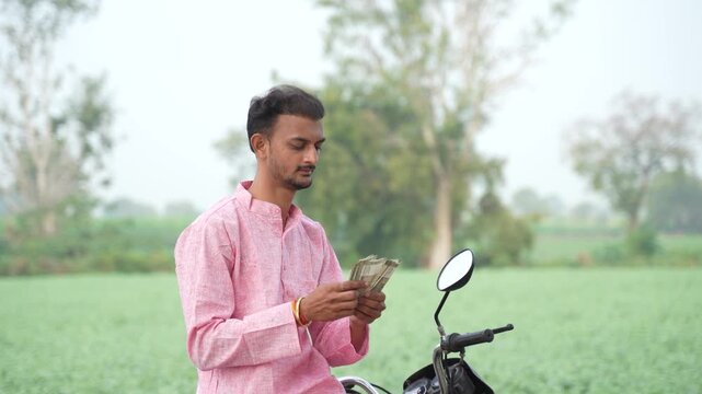 Young Indian farmer counting money at agriculture field