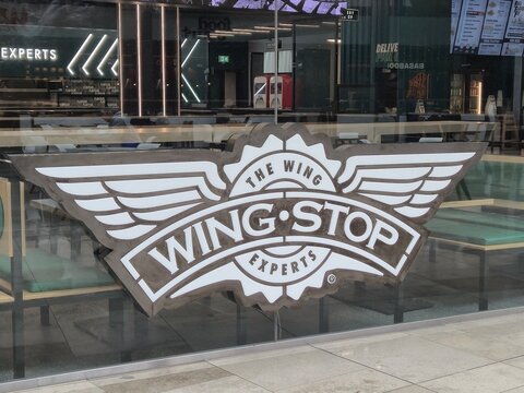 London, UK - 07.07.2025 Wingstop restaurant logo with white wing design displayed on a glass window, showing the interior of a modern fast food location specializing in chicken wings