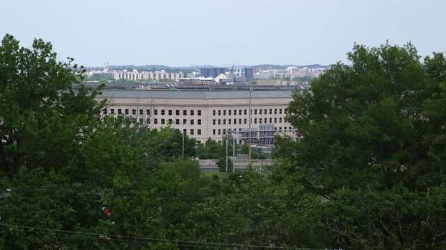 Telephoto view of the Pentagon in Arlington, Virginia framed by trees, showing the Department of Defense headquarters on an overcast day near Washington, D.C.