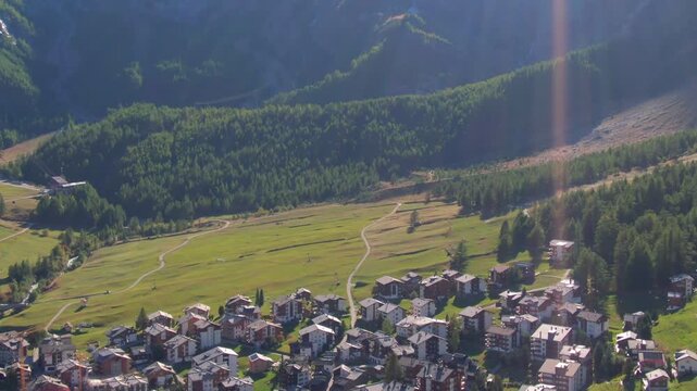 Bird's-eye view of a sunlit Swiss mountain village, traditional chalets, and winding paths
