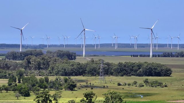 Telephoto 7x view of wind turbines beyond a lake with a high voltage transmission tower in the foreground.
