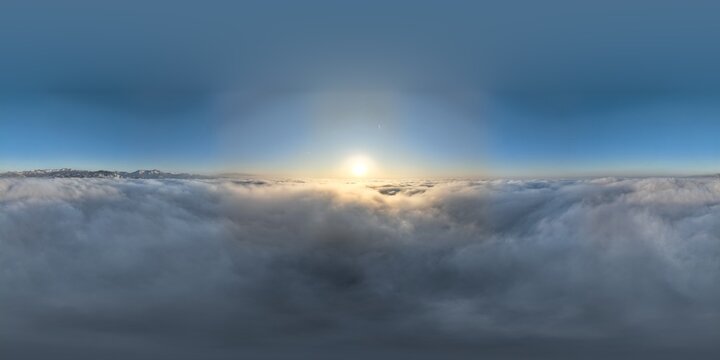 A breathtaking 360 degree equirectangular drone view from high altitude, showing a vast sea of white clouds with distant mountain peaks and a bright sun on the horizon in Georgia.