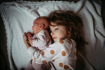 Young girl holding newborn sister. Tender sibling moment.