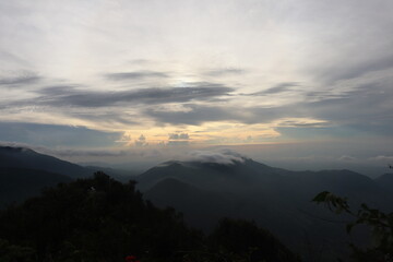 Obraz premium A mountain viewpoint during sunset with dramatic cloudy sky and layered hills, capturing peaceful adventure and travel atmosphere