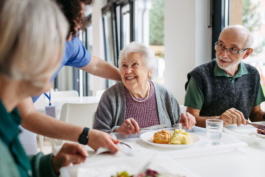 Caregiver serving lunch to elderly residents in a care home.