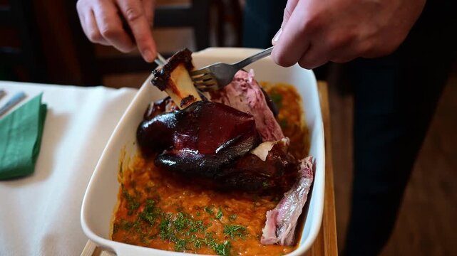 Waiter carving a roasted smoked pork knuckle with beans