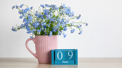Blue forget me not flowers in a ribbed pink mug with a wooden block calendar showing the date June 9, representing spring and anniversaries