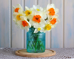 Daffodils bouquet featuring white petals and bright orange or yellow trumpets standing in a turquoise ribbed glass vase filled with water celebrating the arrival of spring