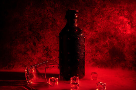bottle of alcohol with a glass and ice cubes on a red background for Valentine's Day
