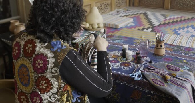 Woman sewing handmade doll with fabric and paints at home workshop
