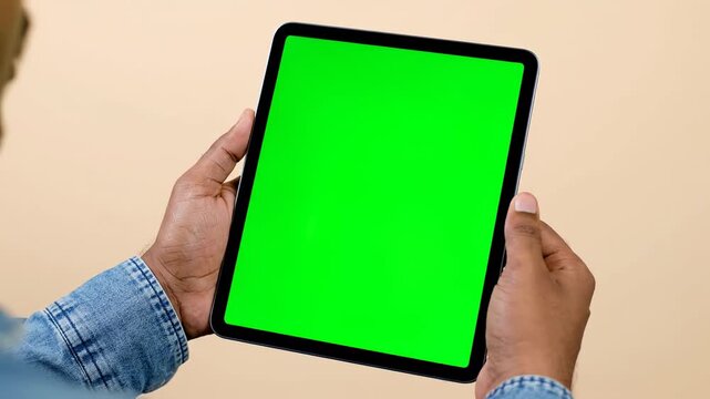 Person holding tablet with green screen mockup, close-up hands, beige background