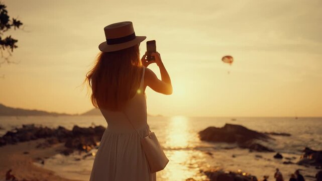 Female vacationer taking picture of paraglider above ocean, summer activity. Carefree woman admiring amazing seascape from coastline in sunset or sunrise, weekend trip to sea, living in resort city
