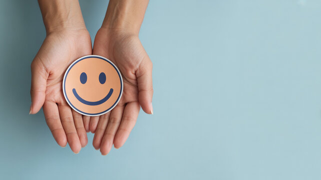 Hands gently cradling a round smiling face sticker against a blue backdrop.