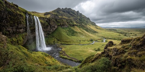 Fototapeta premium Majestic waterfall cascading down rocky cliffs surrounded by lush green hills under a dramatic cloudy sky in a serene landscape of nature's beauty