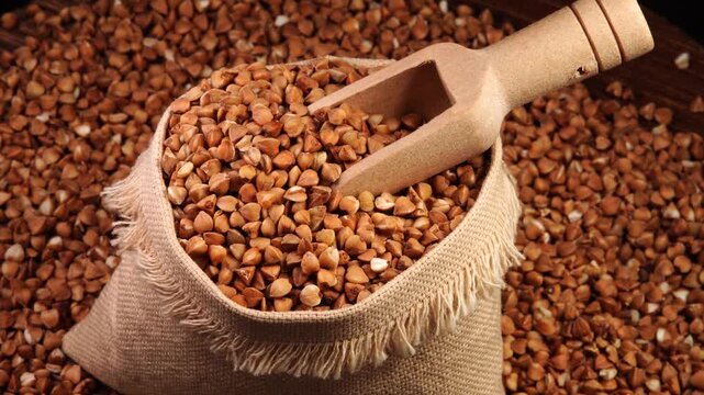 Rotating handmade pouch filled with buckwheat groats and a wooden scoop, close-up.

