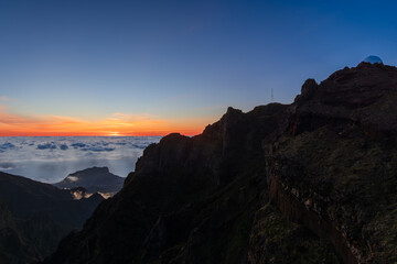 Fototapeta premium Dawn scene from Pico do Areiro viewpoint Madeira Portugal shows observatory dome silhouette, glowing horizon contrasts dark volcanic slopes and floating clouds below