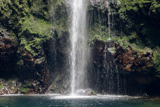 Caldeirao Verde Waterfall curtain splashing into emerald pool on Madeira island, Portugal. Close view of falling water and mossy cliff with wet basalt