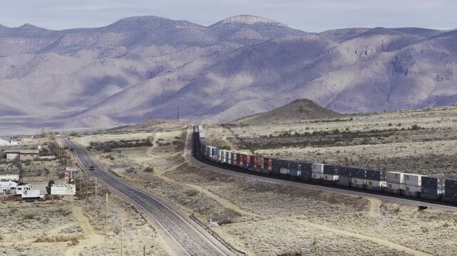 Aerial of shipping containers on train in Arizona desert near Kingman with mountain backdrop