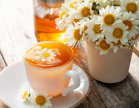 Hot chamomile tea in a white ceramic cup with fresh daisy flowers on a rustic wooden table