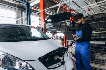 Mechanic using laptop diagnosing electric car