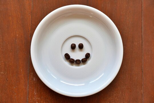 Coffee beans arranged into a smiling face on a round white plate, creative concept for happiness, energy, and caffeine lifestyle