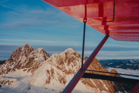 Snow-covered mountain peaks rise beneath the wing of a small aircraft.