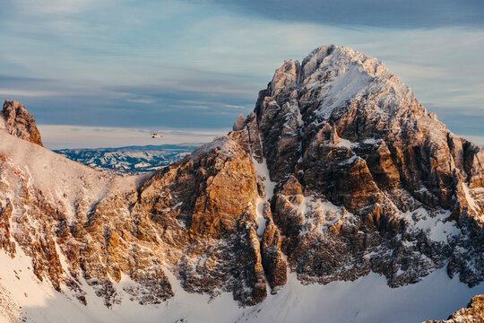 A small plane flies against a rugged mountain ridge in winter during.