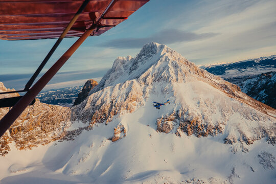 An aircraft wing frames a dramatic snow-covered mountain peak.