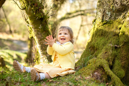 Happy toddler sitting by mossy tree in woodland.