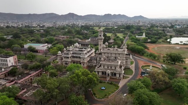 Drone circles around Mayo College heritage building with clock tower surrounded by Aravalli hills. The college was named after Earl of Mayo, Viceroy of India under British rule