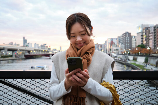 Smiling person using smartphone outdoors by the Sumida River in Tokyo