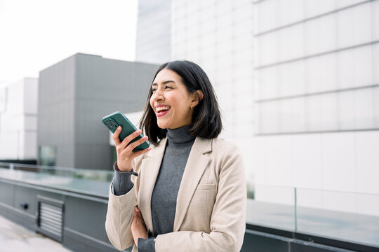 Happy businesswoman standing outside in financial district talking on mobile phone