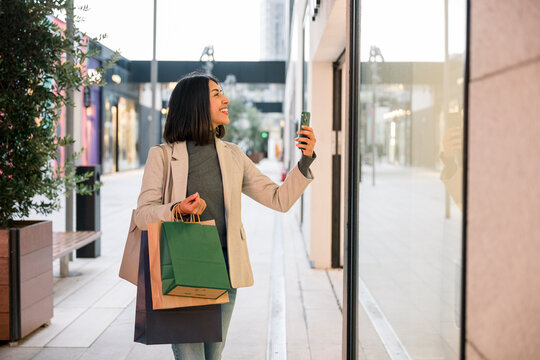 Happy consumer holding shopping bags and taking photo with mobile phone