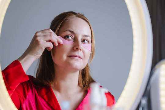 Woman applying under eye patches in front of mirror at home