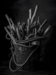 Dark Still Life of Wooden Sticks and Rope in Metal Bucket