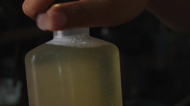 4K Close-up hand holding small bottle filled with liquid on dark background. Minimal lifestyle concept with copy space suitable for beverage skincare cosmetic or product packaging themes.