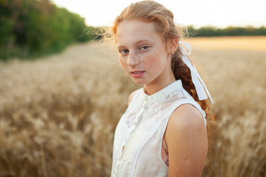 Portrait with red hair and freckles in a wheat field at sunset