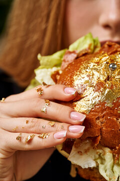 Luxury gastronomy: Close-up of a woman eating a gourmet burger covered in edible gold leaf